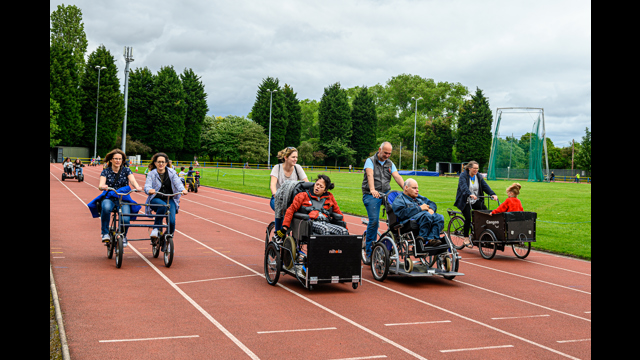 Many people on various types of bike cycling around an athletics track