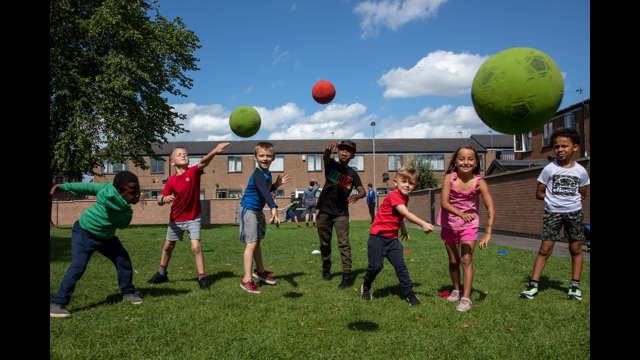 Group of young people in a residential area smiling and throwing balls in the direction of the camera