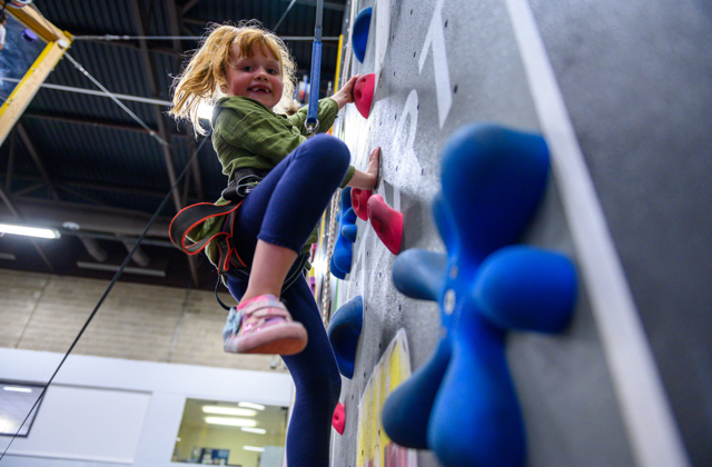 Young girl climbing up an indoor climbing wall smiling at the camera