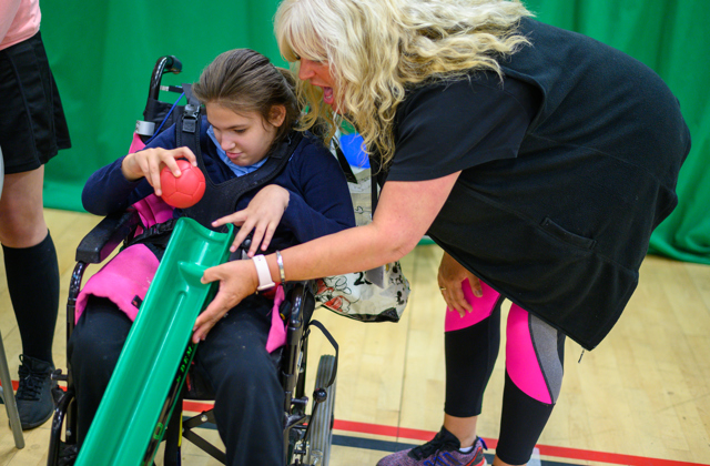 Woman helping a girl in a wheelchair play boccia using a ramp